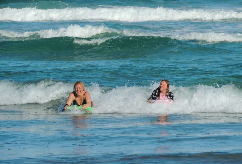 A mom and daughter ride boogie boards in the ocean surf is fun thing to do at any of Rhode Island's beautiful beaches.
