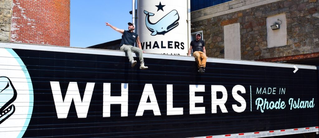 Photo of two men on top of the Whalers sign at Whalers Brewery in Rhode Island. 